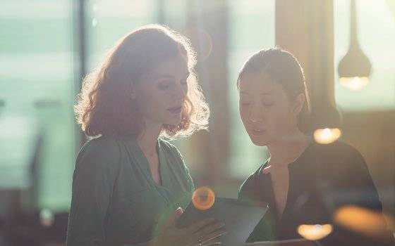 Two women in soft focus look over a tablet device as downlights glimmer in the foreground.
